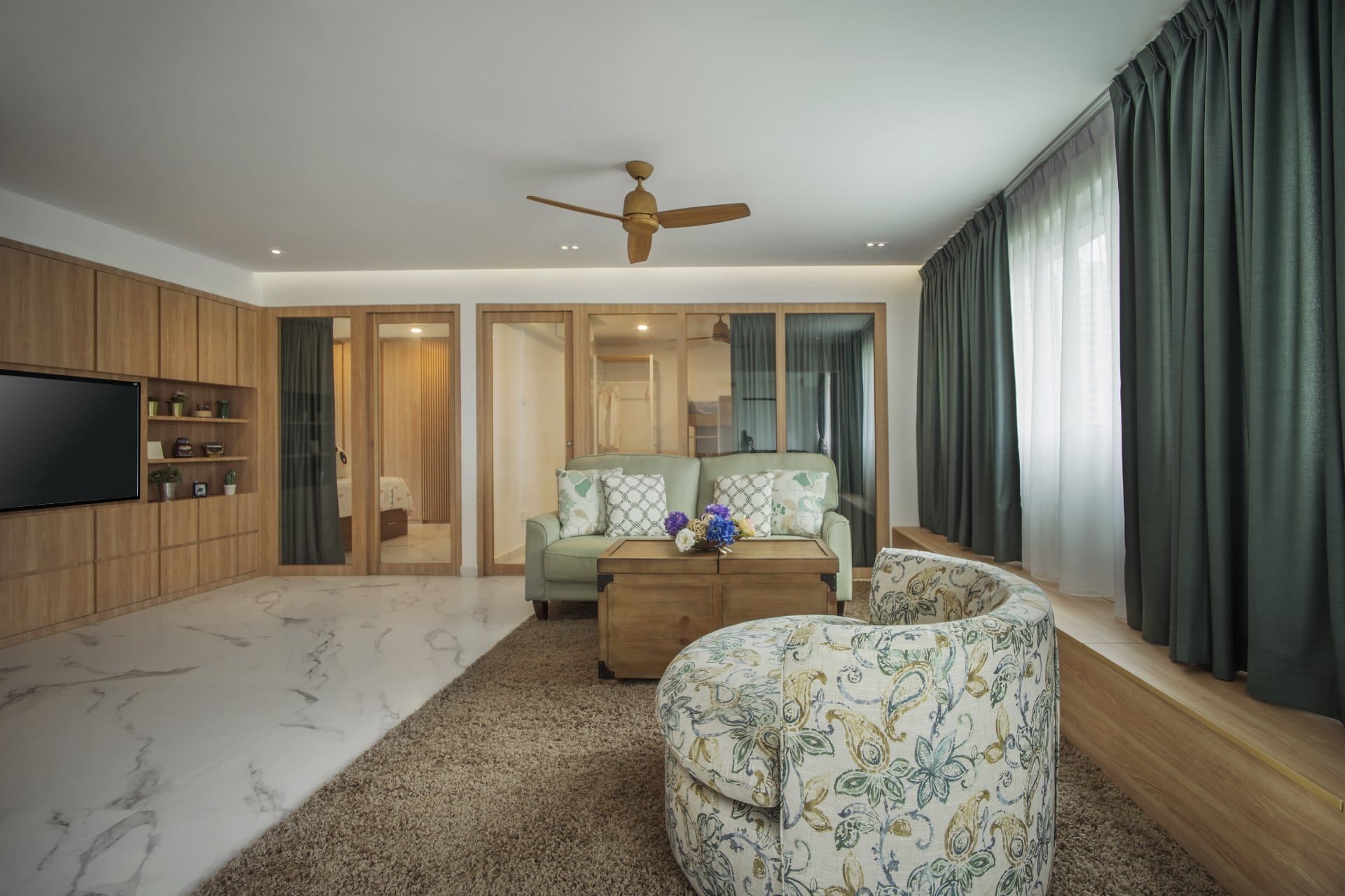 Modern living room with green sofa, patterned armchair, wood ceiling fan, and built-in storage