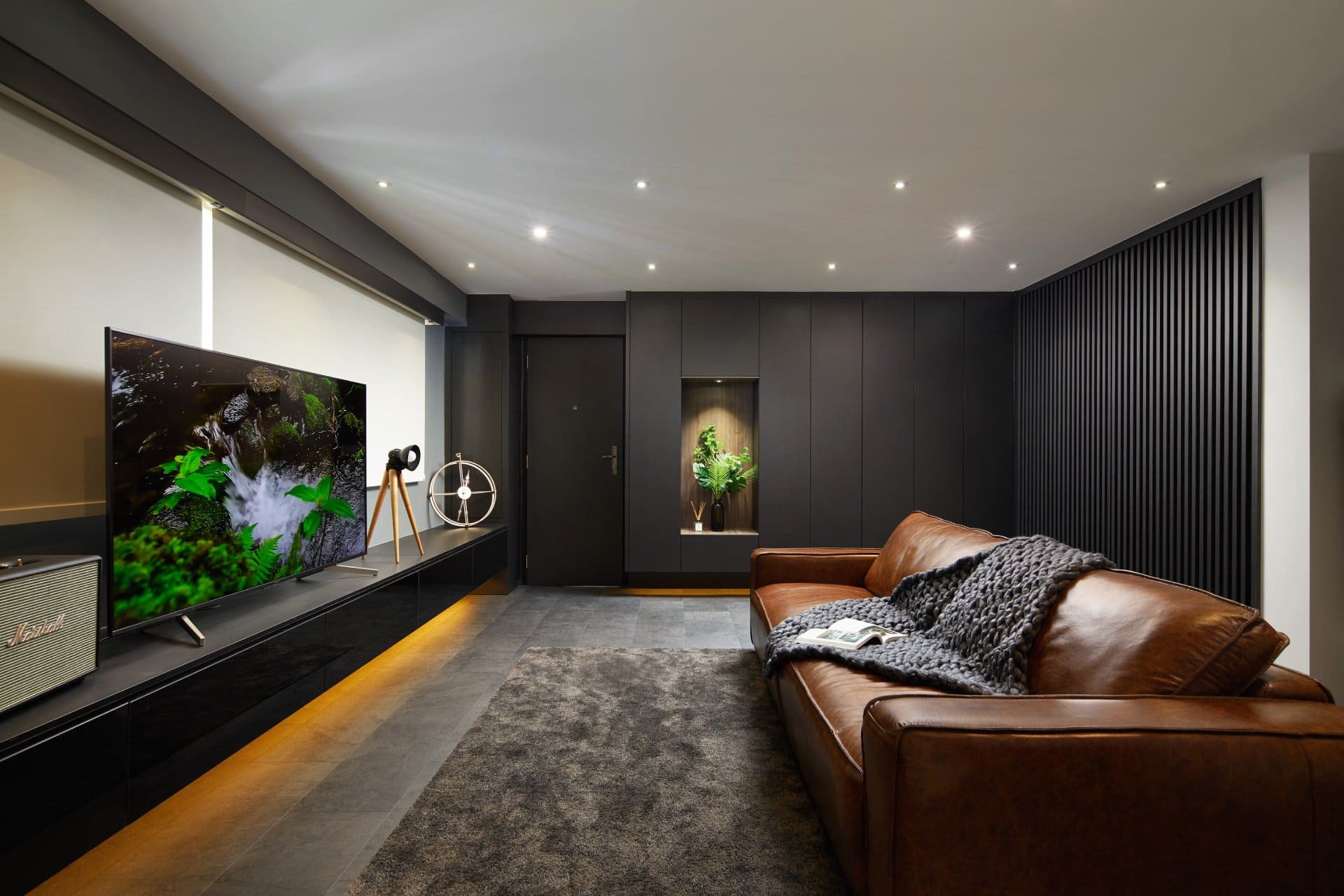 Modern living room with brown leather sofa, large TV, and dark wood paneling