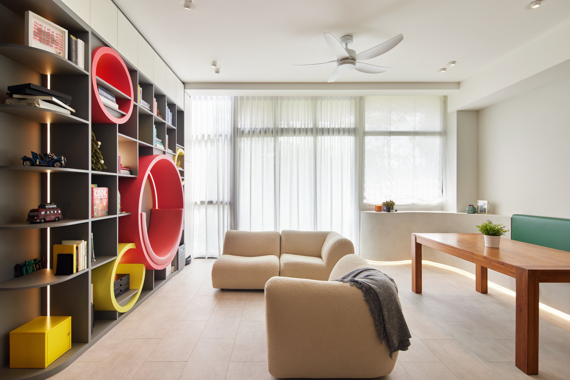 Playful modern living room with curved cream sofas, unique round bookshelf, and a dining nook