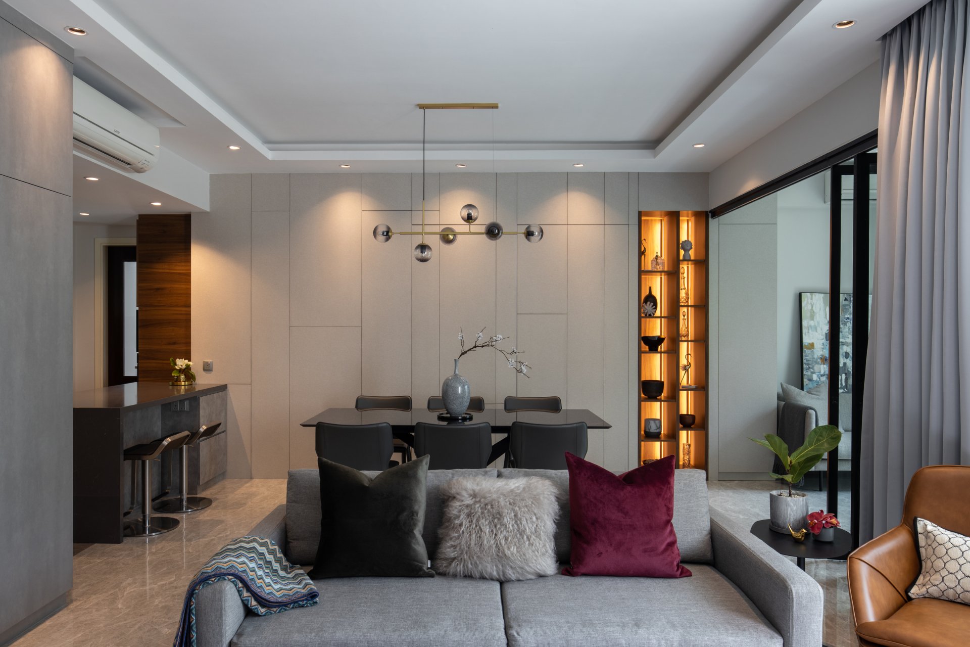 Modern condo living and dining room with grey sofa, pendant lighting, and built-in display shelves