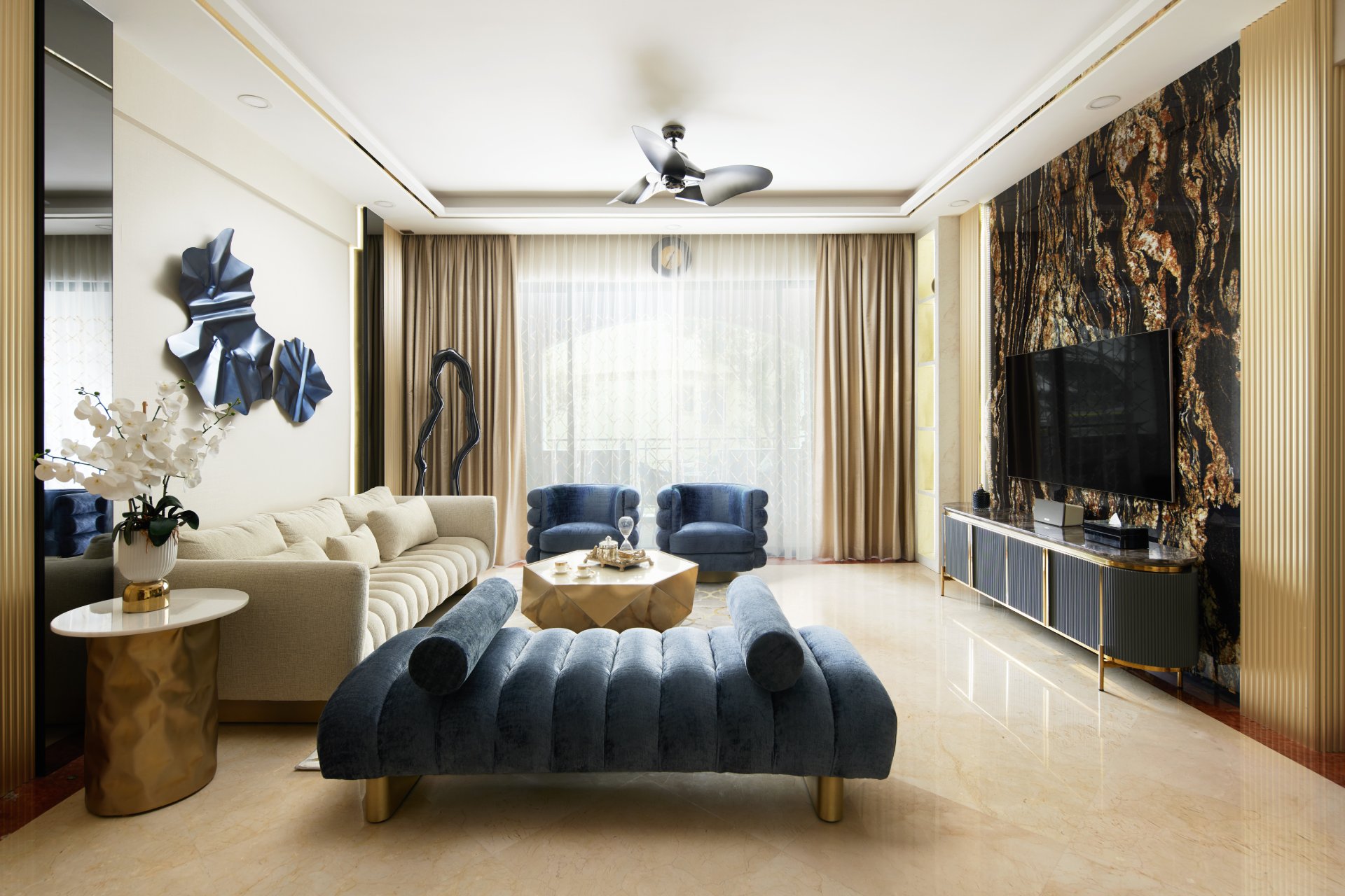 Modern luxe living room with cream sofa, blue velvet chairs, gold accents, and marble TV wall