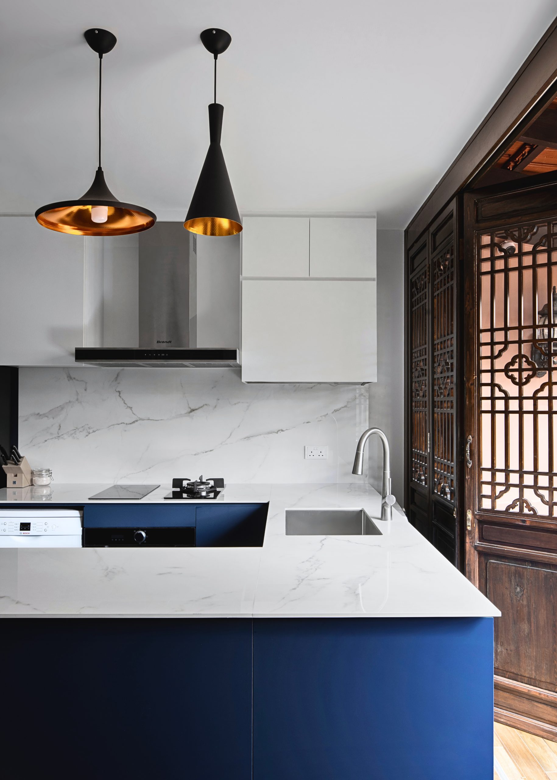 Modern kitchen with navy island, marble surfaces, and oriental wood screen