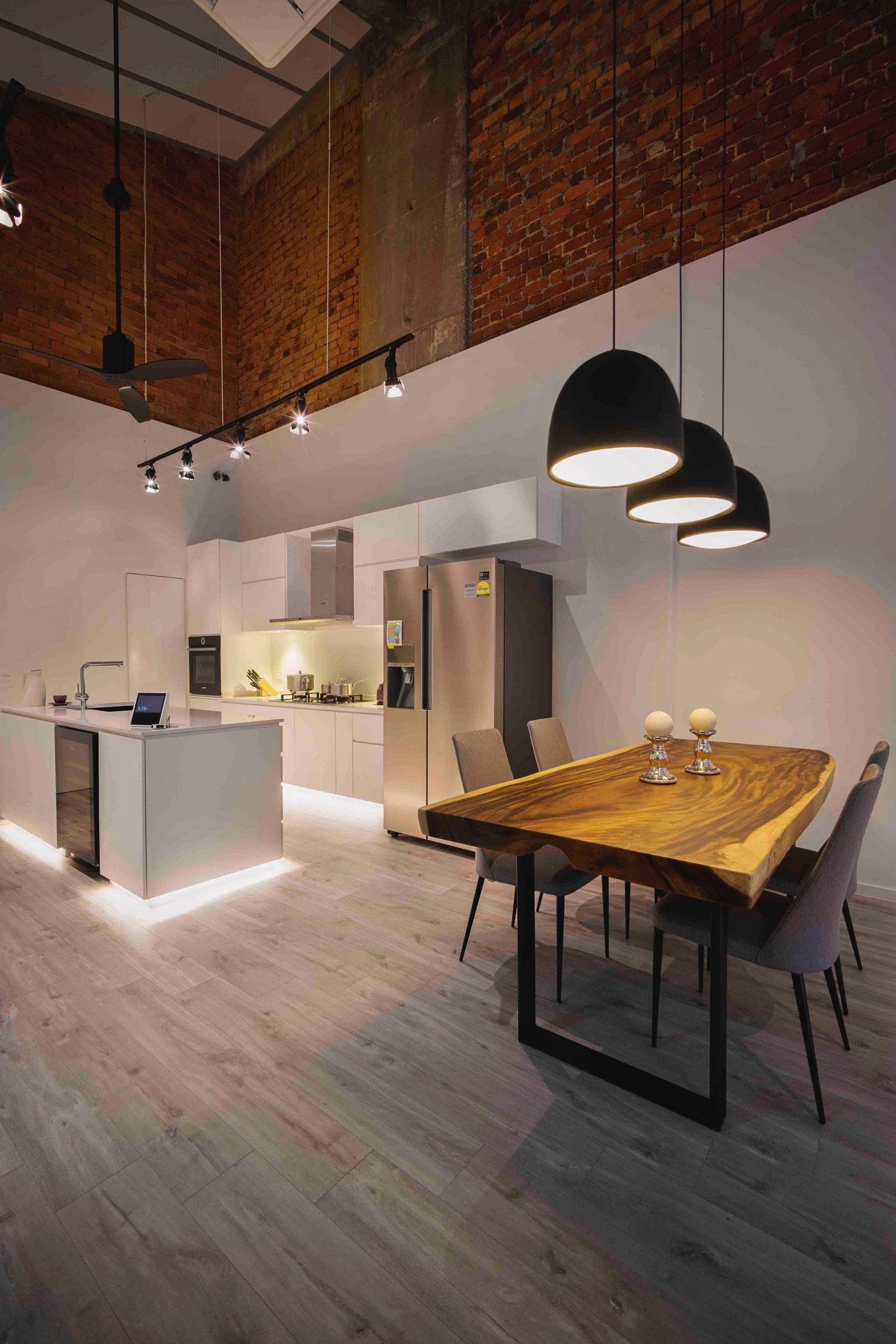 Dining area with natural wood table, pendant lights and exposed brick wall overlooking a white modern kitchen